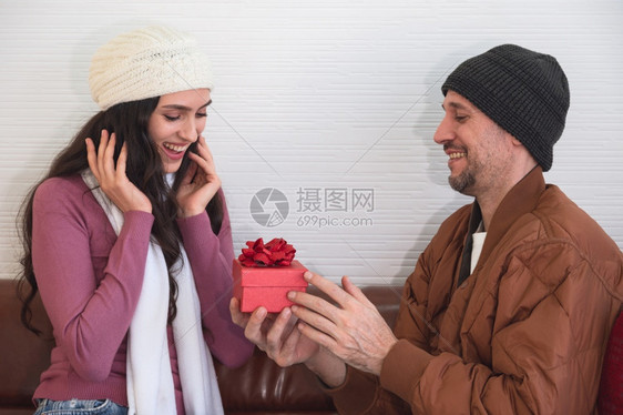 幸福男朋友白种人在客厅沙发上用红色礼物盒在睡椅上给女朋友带来惊喜一起庆祝节日周年或生在家过图片