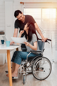 车祸后坐在轮椅上的妇女在家中与她的爱人一起使用计算机工作相互照顾的概念和新技术使残疾人在社会中享有平等地位一社会中的平等工人聪明图片
