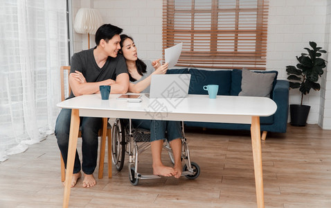 车祸后坐在轮椅上的妇女在家中与她的爱人一起使用计算机工作相互照顾的概念和新技术使残疾人在社会中享有平等地位一社会中的平等禁用随意图片
