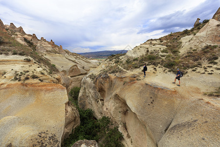 古老的石灰一种多云的天空和山景背下一对年轻的游客在卡帕多西亚的峡谷边缘检查深一对年轻的游客站在卡帕多西亚的峡谷边缘图片