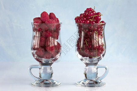 黑加仑猩红蓝色的将草莓和红沙律倒入透明杯拿铁的子并排成一在浅蓝色背景上站立把草莓和红色卷曲放在一个清晰的杯子中淡蓝色背景上图片