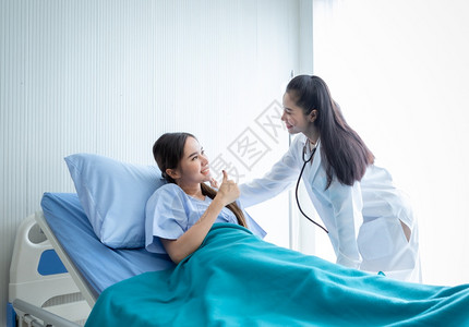 症状生病的孕亚洲年轻女病人在床上展示拇指与微笑脸的相容对医院背景中的亚洲年轻女医生来说图片