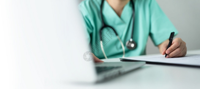 专业的亚洲人穿绿色制服的护士或外科医生亚洲女护士或外科医生在笔记本电脑上工作并在剪贴板和医院疗室黑笔纸的档案核对清单中写一些病人图片