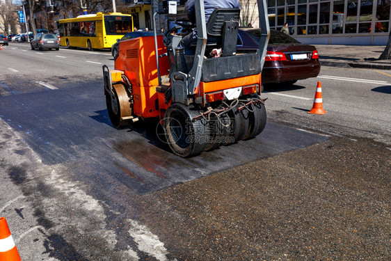 筑路工一条重橙色振动横轴压板在一条有交通锥形栅栏的市区街道上铺平一段路面用复印空间图像制对市街路段道进行修补理铺沥青图片