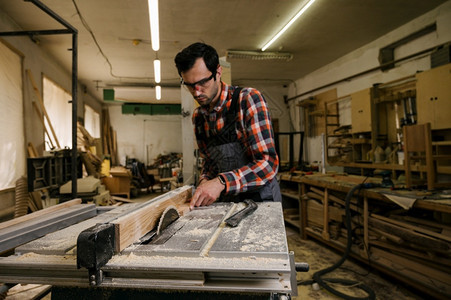 车间A保持木工车间的作流程木车间作服的人在锯木厂使用床切割木板的匠专业工概念车间的作流程艺图片