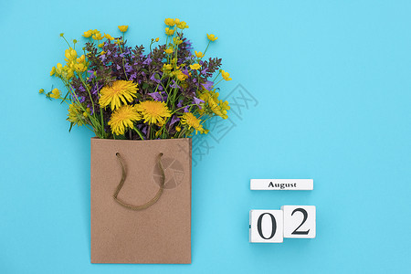 约定乡村铺设Wooden立方体8月2日历和蓝背景的手工艺品包中富彩的生化花朵蓝色背景的GreetingcardFlatLay概念图片