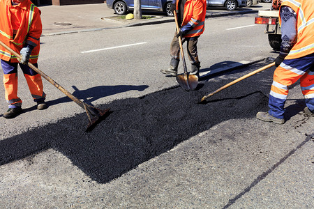 摄影铲筑路工作队在部分道路上堆放新鲜沥青并平整以便在道路施工中进行维修人大队在道路施工中用铁锹清理部分沥青碎石图片