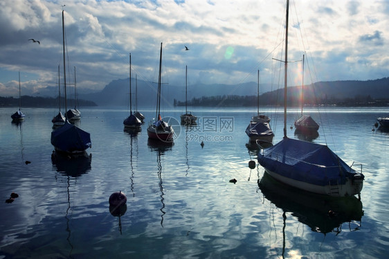 云桅杆锚定一群帆船停靠在码头附近正如太阳开始使Lens照明耀斑可见时一样这些帆船正在瑞士卢塞恩Lucernne拍摄图片