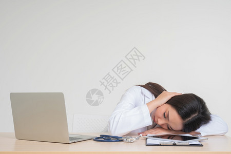 亚洲人女脸年轻的亚洲女医生坐在办公桌旁由于过度工作精神压力疲劳的概念和医生责任她看起来不快乐和疲倦处理沮丧的病情图片