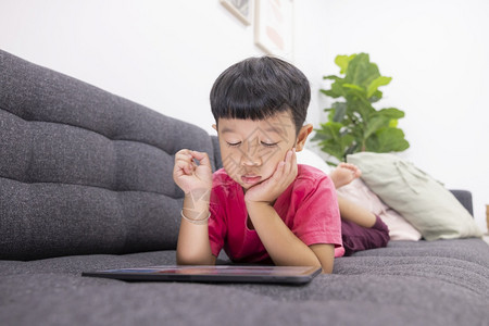 就寝时间网络微笑的小男孩看着在客厅舒适沙发上的触摸板享受在数字平板电脑上玩游戏的乐趣利用有的应程序来玩乐小孩子游戏在线的图片