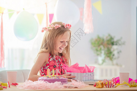 微笑希望可爱的小女孩在生日礼物上拆解孩子是快乐和兴奋的生日派对白种女孩是梦想般的笑容看着生日彩虹蛋糕花样多的背景与气球生日派对和图片
