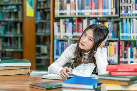 年轻的困韩国人亚洲青年学生穿便衣在木制桌子上阅读并在大学图书馆或架上的群落中阅读各种书籍回到学校概念内图片