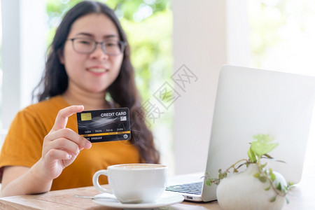工作场所女自由职业者商余休闲女摘要模糊不清重点为显示持有信用卡在咖啡店笔记本电脑工作如背景在线购物和支付卡片营销图片