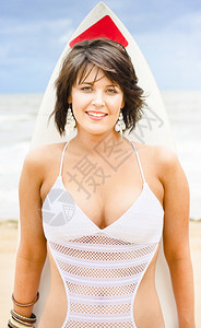 在享受热带海滩上的阳光和暑假度时站在海洋前线的冲浪委员会中持着她的冲浪水面板妇女娱乐海岸常设图片
