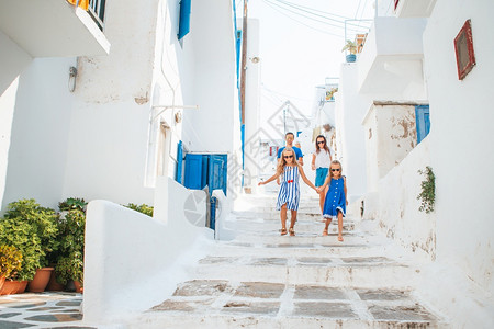 狭窄的白色旅游家庭在欧洲度假父母和孩子在米科诺斯岛典型的希腊传统村庄街道上白色墙壁和五颜六的门在希腊欧洲家庭度假图片