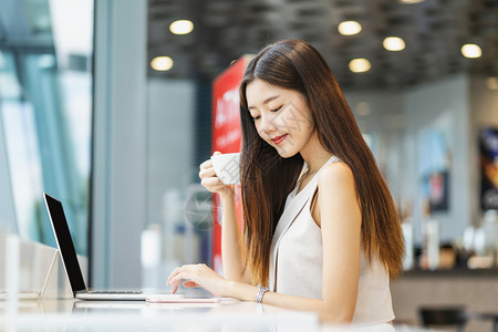 现代的共同工作药片亚洲年轻女持有一杯咖啡在现代店或合用空间使带有技术笔记本电脑的移动话技术智能移动和潮时生活方式企业家概念等亚洲图片