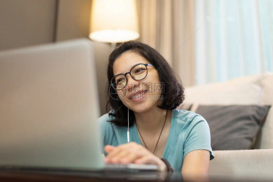 穿着蓝衬衫和眼镜的亚洲美丽女孩她们享受在线课程互联网无线技术快乐笑的年轻女在隔离期间使用笔记本电脑与家隔绝时使用手提电脑Covi图片