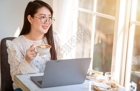 白色的马克杯吸引人女商用笔记本电脑和咖啡店智能手机商业生活方式交流概念与笔记本电脑和智能手机一起工作的零用笔记本散工图片