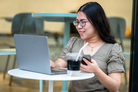 商业女人用笔记本电脑与咖啡杯一起工作在咖啡馆商务生活方式上撰写关于智能手机临时空闲消息的讯电话保持自由职业者图片