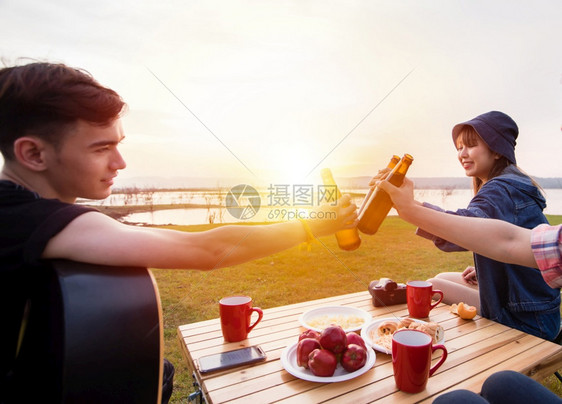 一群亚裔朋友在日落时湖附近露营旅游饮酒啤弹吉他与夏月快乐一起欢男人马克杯咖啡图片