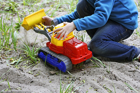 儿童在新鲜空气中玩耍一个儿童坐在沙地和草之间幼小孩子的景象就是坐在沙地里玩着一辆大具车只要潮湿多云的图片