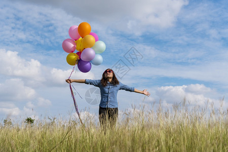 女人拿着气球在绿色草地白云和蓝天空上奔跑快乐轻松的天空手拿着充满活力的空气球在生日派对上欢快的盛宴玩自由美丽的图片