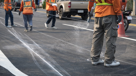 维护尽管公路工人小组的低正致力于在沥青道路上绘制交通彩色线标记同时仍在城市周围行驶重点放在前方的人身上以男子为主车辆图片