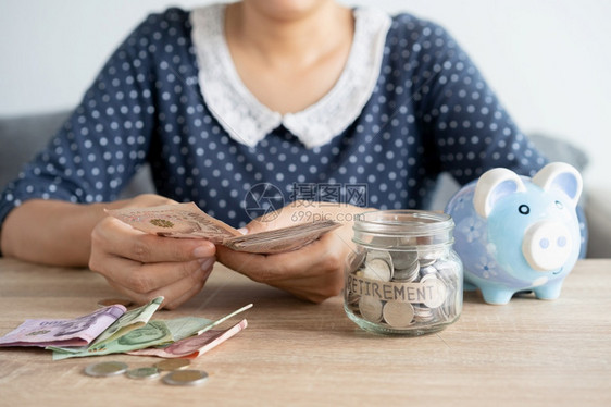 数亚洲妇女当家桌边计票时手握的亚洲妇女投资企业和退休公司用玻璃瓶子小猪银行融资和为未来概念储蓄资金的方式在桌上计算钞票支付经济图片