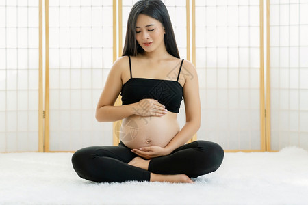 期待亚洲怀孕妇坐在日本风格的房子里坐着并握手肚子的亚洲孕妇在白色地毯上的怀孕概念准备健康地做母亲运动孩子图片