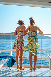 两个年轻女孩朋友姐妹站在渡轮或乘船前往岛旅游目的地暑假渡轮或船甲上的围栏旁在阳光明媚的白天望着地平线太阳镜帆船海图片