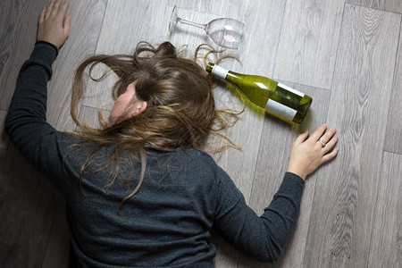 言难而上宿醉酒的年轻女孩躺在地板上因为喝红酒空玻璃和瓶子而感到