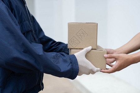 帖子劳动贮存包裹交付概念白橡皮手套和轻重量黑蓝大衣的邮递员将两件小包裹交给他的客户图片