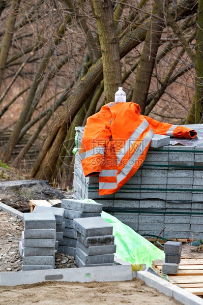 石工在春天的一公园树木的背景下在一堆铺路板附近的建筑工地上橙色建筑夹克垂直图像复制空间建筑商的橙色夹克躺在一堆铺路板上背景是公园图片