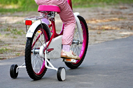 娱乐女孩骑着粉红子的自行车在铺路面上铺砌车辆图片