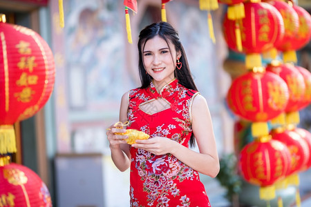身穿红色传统青相的亚洲妇女拿着金钱袋上面写着字母祝福的纸灯是新年幸运赞美奖章注幸福亚洲人年轻的肖像图片