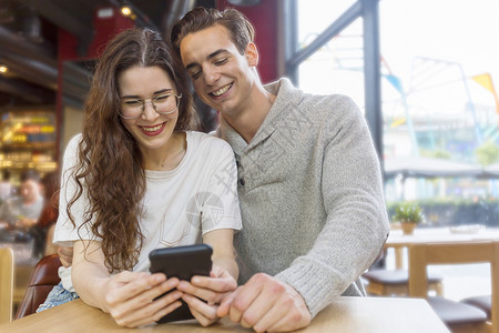 室内的联系家有趣情侣或婚姻分享智能电话观看媒体内容在餐厅里坐着图片