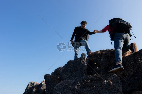 男女的背包手正在攀山一个男人伸着手拉女上来成功登山夫妻团队合作很好两人都在一帆风顺地爬了2号山顶上背包客一种女图片