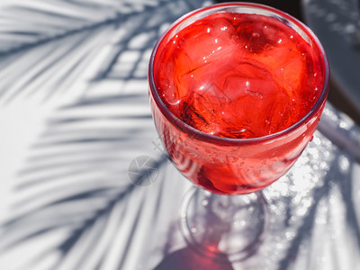 红酒杯饮料色的美丽葡萄酒杯有粉红鸡尾酒和冰块站在白板上靠着棕榈叶的阴影站立在白板上最接近的景色更休闲概念与美丽玻璃搭配粉红鸡尾酒图片