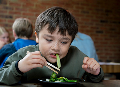 美味的饥饿桌子健康儿童男孩使用牵着PakChoi和TenderstemBroccoli的叉棍用牡蛎酱和大蒜煎熟了Kid在日本餐馆图片