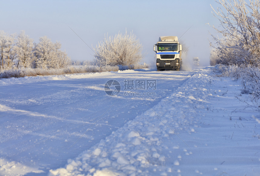 清晨一支重型卡车队沿雪覆白的色小路行驶沿一条有银冻霜的灌木丛一带被雪覆盖的白色小路行驶由一辆重型卡车组成的队沿一条雪白小路行驶后图片