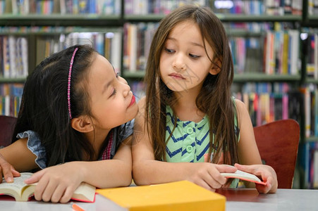 教学女儿侮辱两个可爱的女孩互相嫉妒同时在图书馆阅读本而教师则授人们的生活方式和教育在学校概念中年轻人友谊和孩子的关系时当面看待他图片