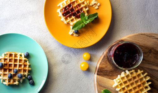 装满罐果酱和蓝莓红黄水果的杜松饼在木制桌上加橘子和绿板刨冰午餐牛奶图片