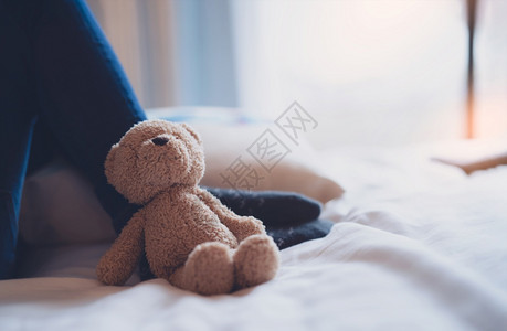 天悲伤的孤独泰迪熊躺在幼小腿上阳光照在窗外萨德棕色与早晨躺在床上Fluffy和模糊背景的玩具国际失踪儿童日国内的闪亮图片