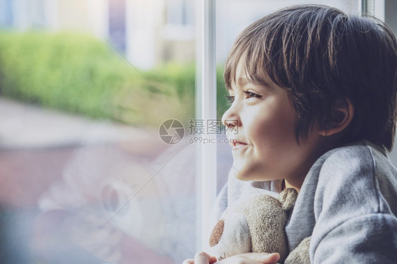 玩具松弛坐在窗户边上写着玻璃的正面男孩带着微笑的脸看窗外在校儿童自己孤立地在家休息Qualrantinecovid19家庭教育远图片