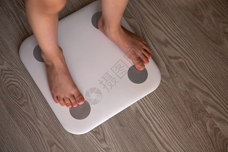 女孩或男子站在白色现代电子智能比例尺上称自己为身高和体重的白人现代电子智能型超标在灰色木地板上站立只有腿是可见的东西重量控制健康图片