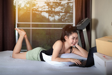 室内的侧面肖像有吸引力的亚洲年轻女在床上躺下家里卧室用笔记本电脑工作从自家概念中工作在家冲扫网络吸引人的包裹图片