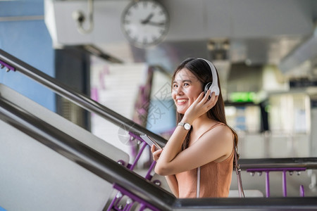 青少年轻亚洲女乘客在大城市通勤和交上旅行时佩戴耳机和使用智能移动电话聆听音乐并走在地铁站的楼梯上如乘坐大城市往返车和交通手机快乐图片