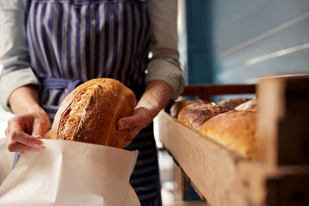 熟食店面包销售助理将新鲜烘烤的有机苏德罗面包饼放入可持续纸袋女士包装图片