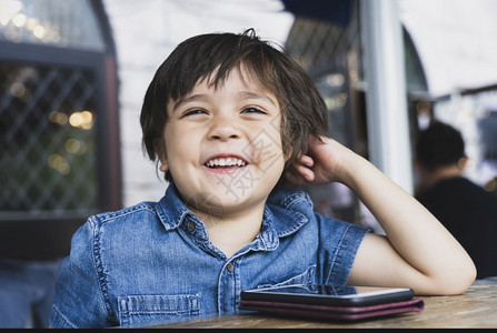 卡通手网络现代的卡通长相快乐孩子带着微笑脸向外看小男孩着木图或手机游戏在咖啡馆里等待食物有技术的儿童概念背景