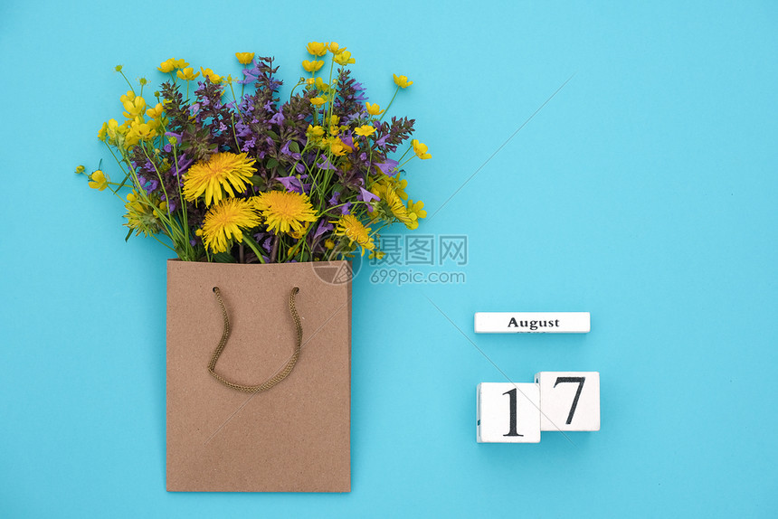 Wooden立方体8月17日历和蓝背景的手工艺品包中现场多彩的生鲜花蓝色背景的GreetingcardFlatLay概念喜好8月图片